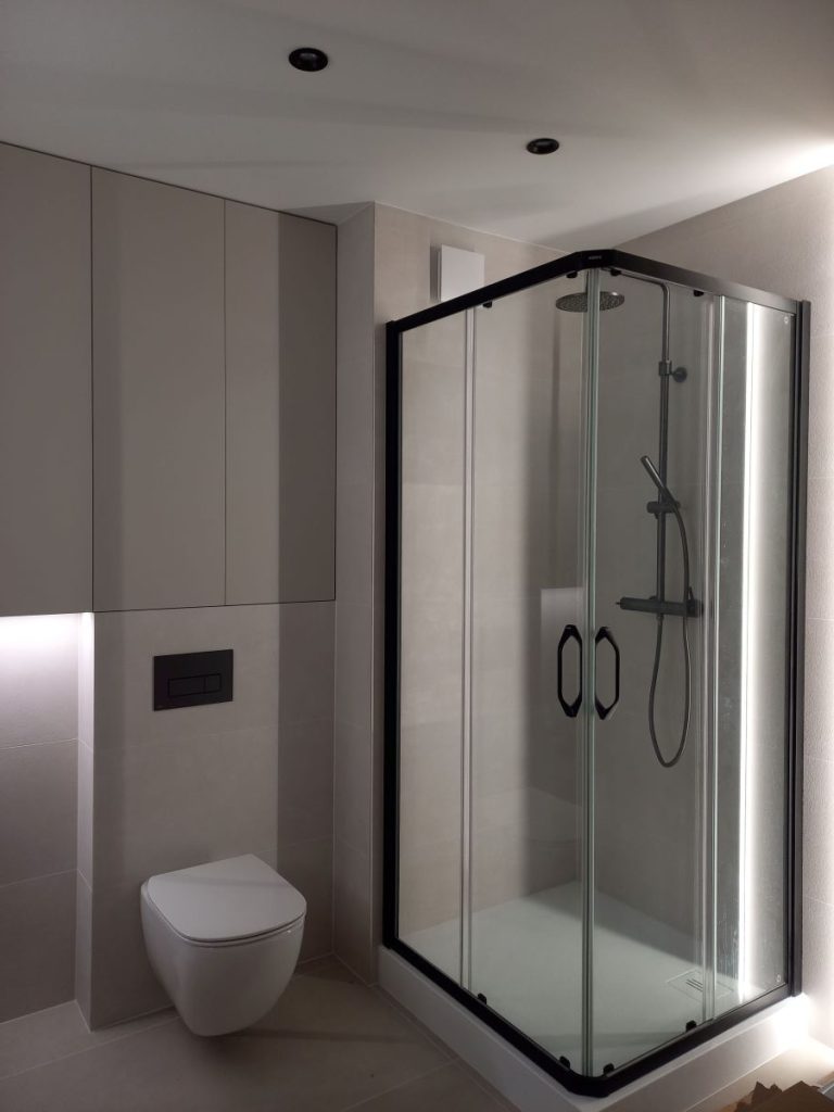 Nowoczesna łazienka, czarna kabina prysznicowa narożna, biała toaleta WC, szare płytki ścienne, minimalistyczny styl.