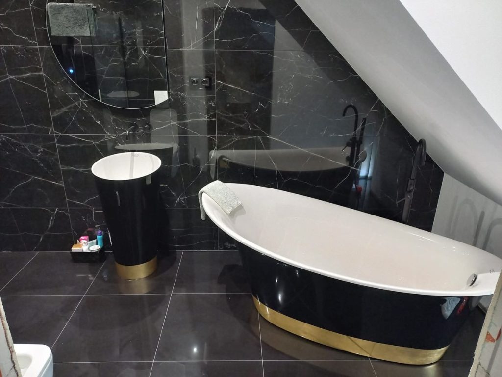 Nowoczesna łazienka w stylu glamour, czarno-złota wanna wolnostojąca, marmurowe płytki, okrągłe lustro.