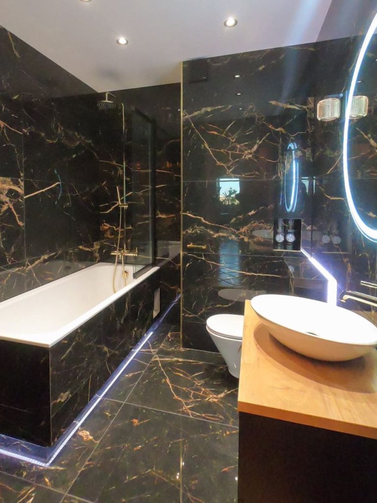 Nowoczesna łazienka w stylu glamour, czarno-złota wanna wolnostojąca, marmurowe płytki, okrągłe lustro.