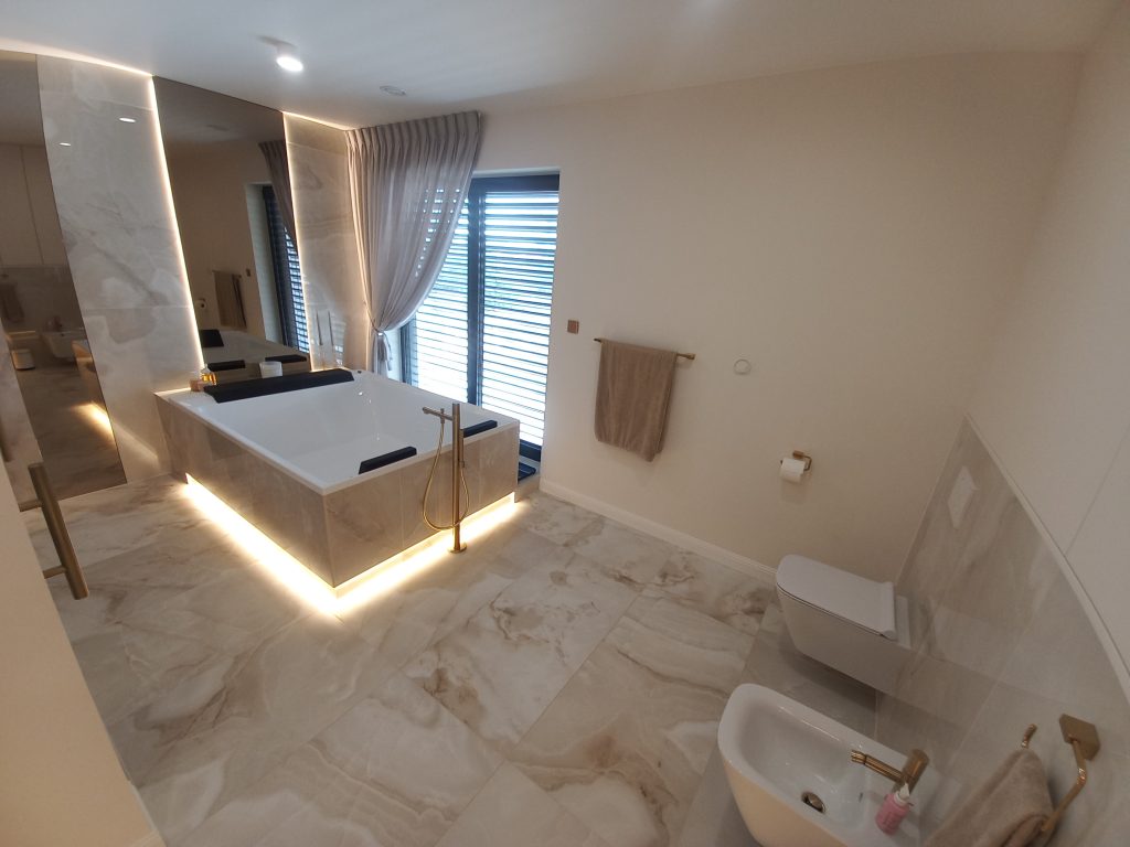 Nowoczesna łazienka w stylu glamour, układanie płytek imitujących marmur, lustro okrągłe LED, złota armatura i dodatki, szafka łazienkowa.