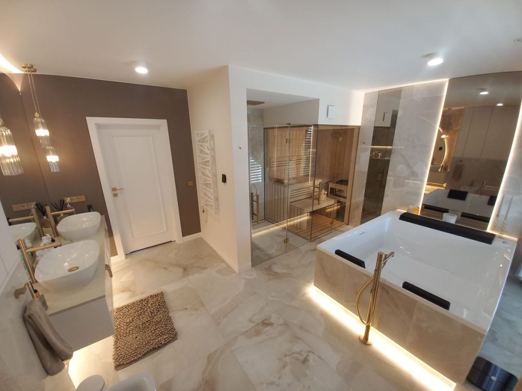 Nowoczesna łazienka w stylu glamour, układanie płytek imitujących marmur, lustro okrągłe LED, złota armatura i dodatki, szafka łazienkowa.