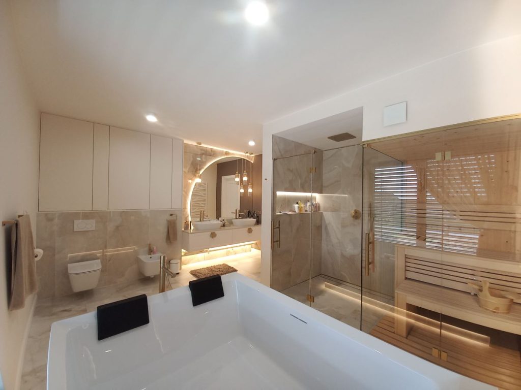 Nowoczesna łazienka w beżowych odcieniach z prysznicem, wanną i drewnianą szafką, zrealizowana przez Adama Kundzika