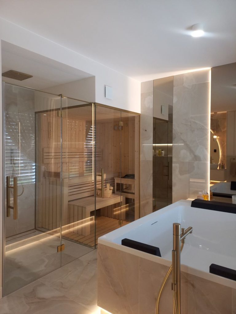 Nowoczesna łazienka w stylu glamour, układanie płytek imitujących marmur, lustro okrągłe LED, złota armatura i dodatki, szafka łazienkowa.